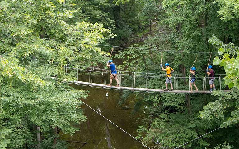 People crossing a bridge while tethered at Common Ground Center 