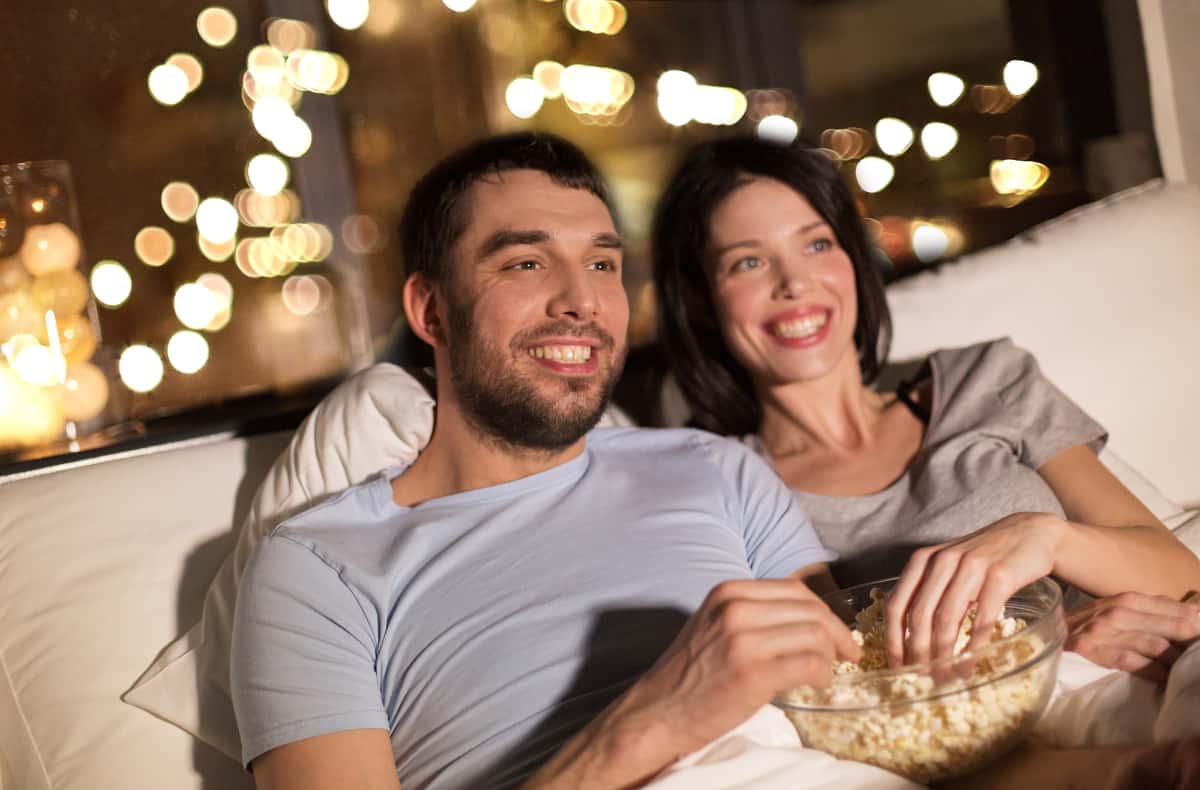 two people sharing a bowl of popcorn on the couch