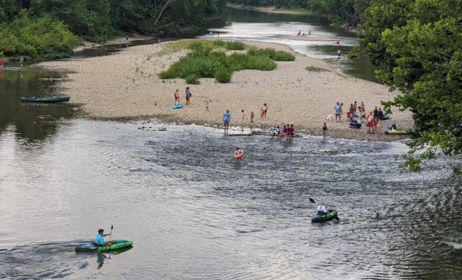 People on a sandy beack and kayaks in the river