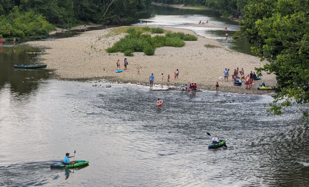 Featured image for our canoe and kayak article - People on a sandy beach and kayaks in the river