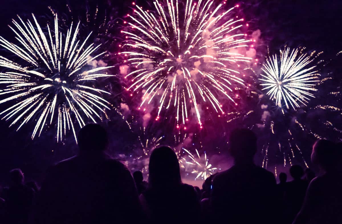 Fireworks going off in a dark sky with a group of people watching
