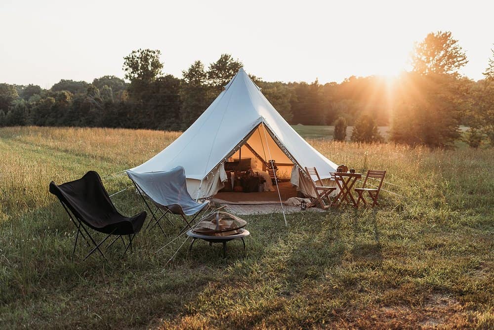 A field with a luxury tent set up , camp chairs, and a fire pit