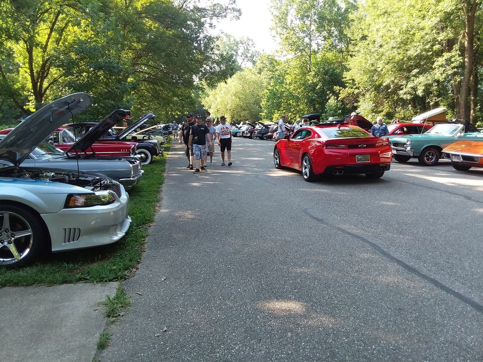 classic car show with cars parked along the sides of a street; people walking up the street
