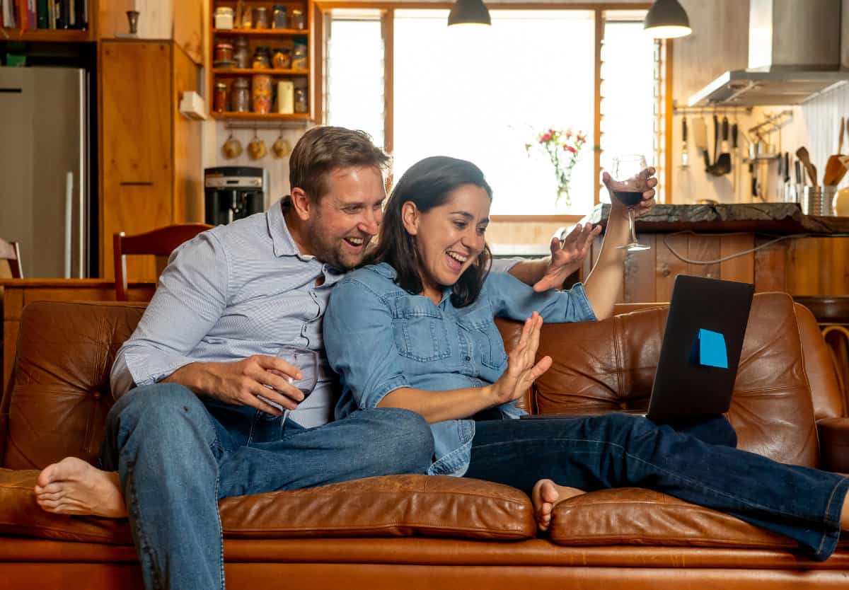 man and woman sitting on a couch enjoying a Zoom call on their laptop