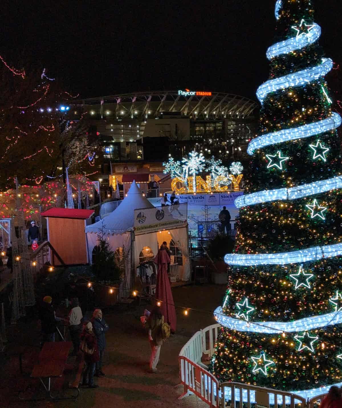 Cincinnati Christkindlmarkt image showing the lighted Christmas tree, skaters on the ice rink, igloos, and people wandering through booths
